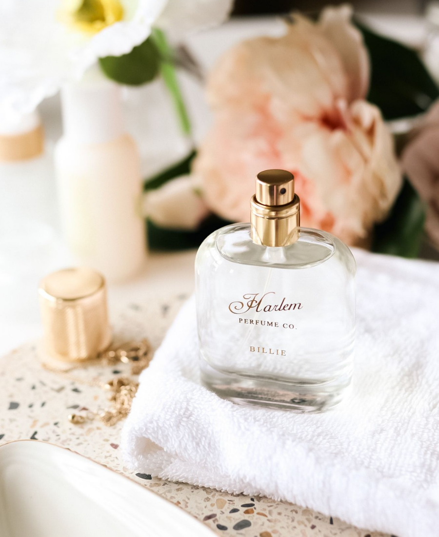 Billie Eau de Parfum bottle on a folded white towel with soft flowers in the background.