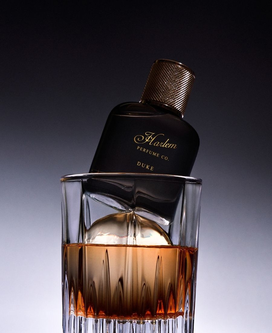 Harlem Perfume Co. Duke perfume bottle with a glass of amber liquid on a gradient background