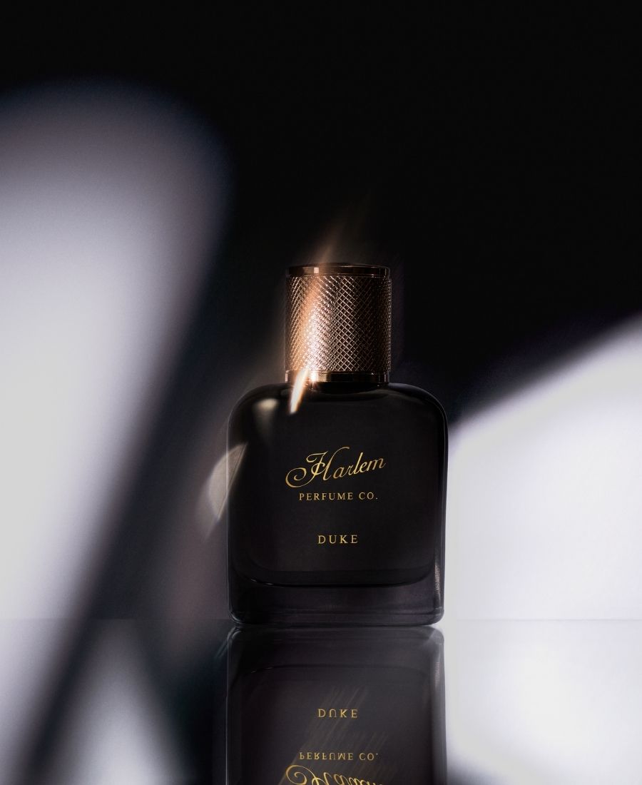 Black perfume bottle labeled 'Harlem Perfume Co. Duke' on a reflective surface with dark background