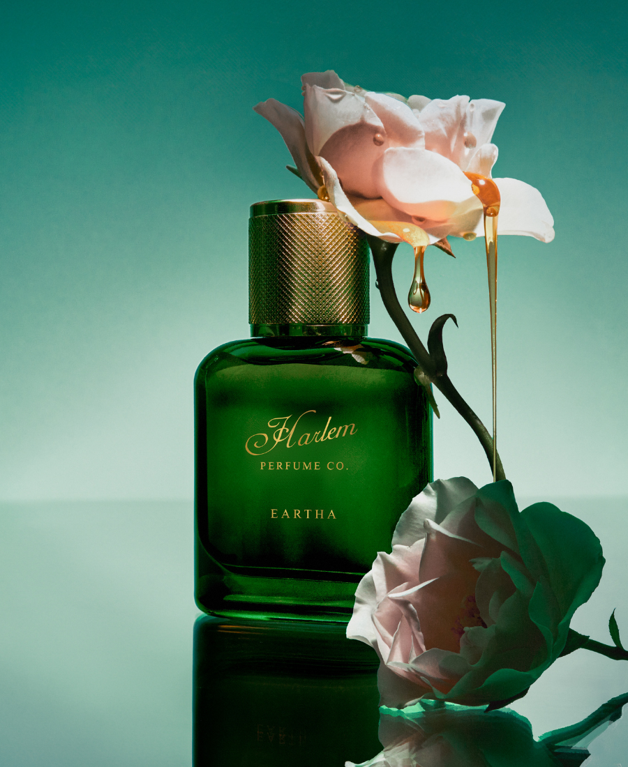 This is an image of the Eartha Eau De Parfum surrounded by pink roses dripping with liquid amber against a teal background.
