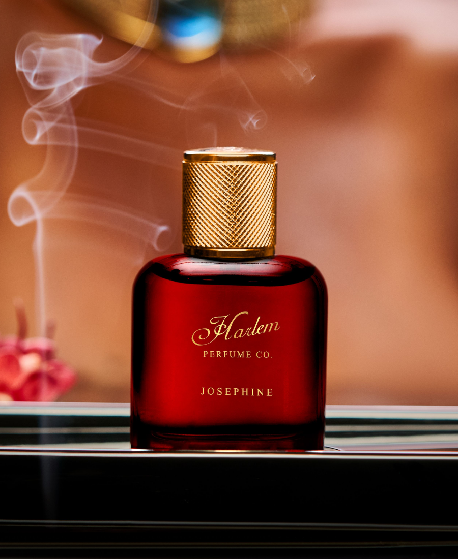 This is a lifestyle image of the Josephine Eau De Parfum on a table against an amber, smokey background.