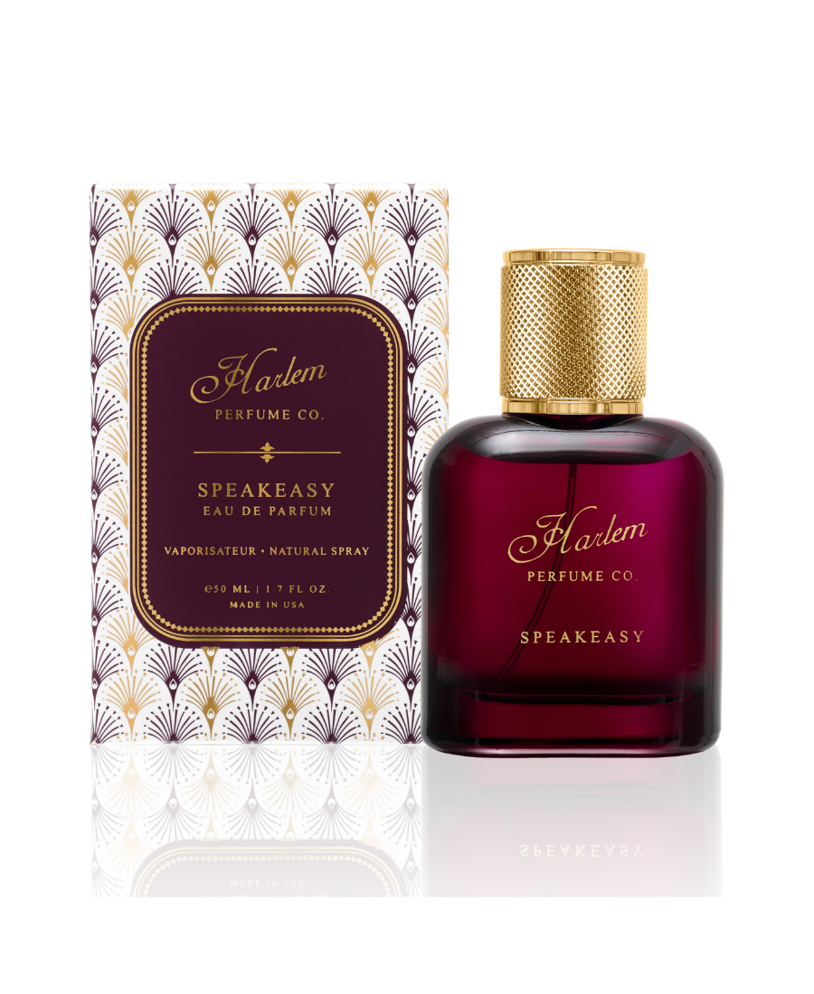 An image of our 50 ml / 1.7 oz Speakeasy eau de parfum in a rich burgundy bottle with a gold cap and the Harlem Perfume Co logo on the bottle with the word Speakeasy in all caps in a block print font. The bottle is pictured next to it's decorative box with a gold, burgundy and white art deco pattern.