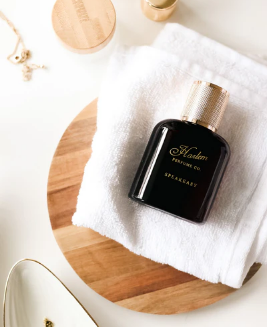 This is a lifestyle image of the Speakeasy 50ml Eau De Parfum bottle laying on a white table with a white towel and wooden and ceramic containers.