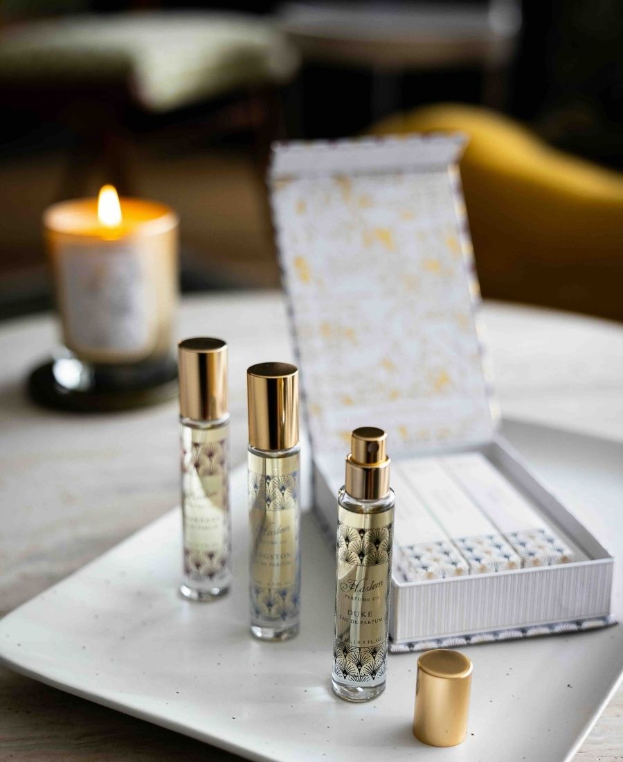 This is an image of three travel size perfume bottles with gold caps on a table next to a lit candle and a decorative box.