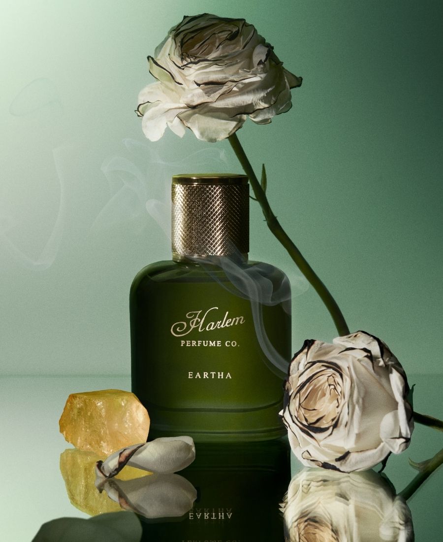 This is an image of the Eartha Eau De Parfum surrounded by pink roses dripping with liquid amber against a teal background.