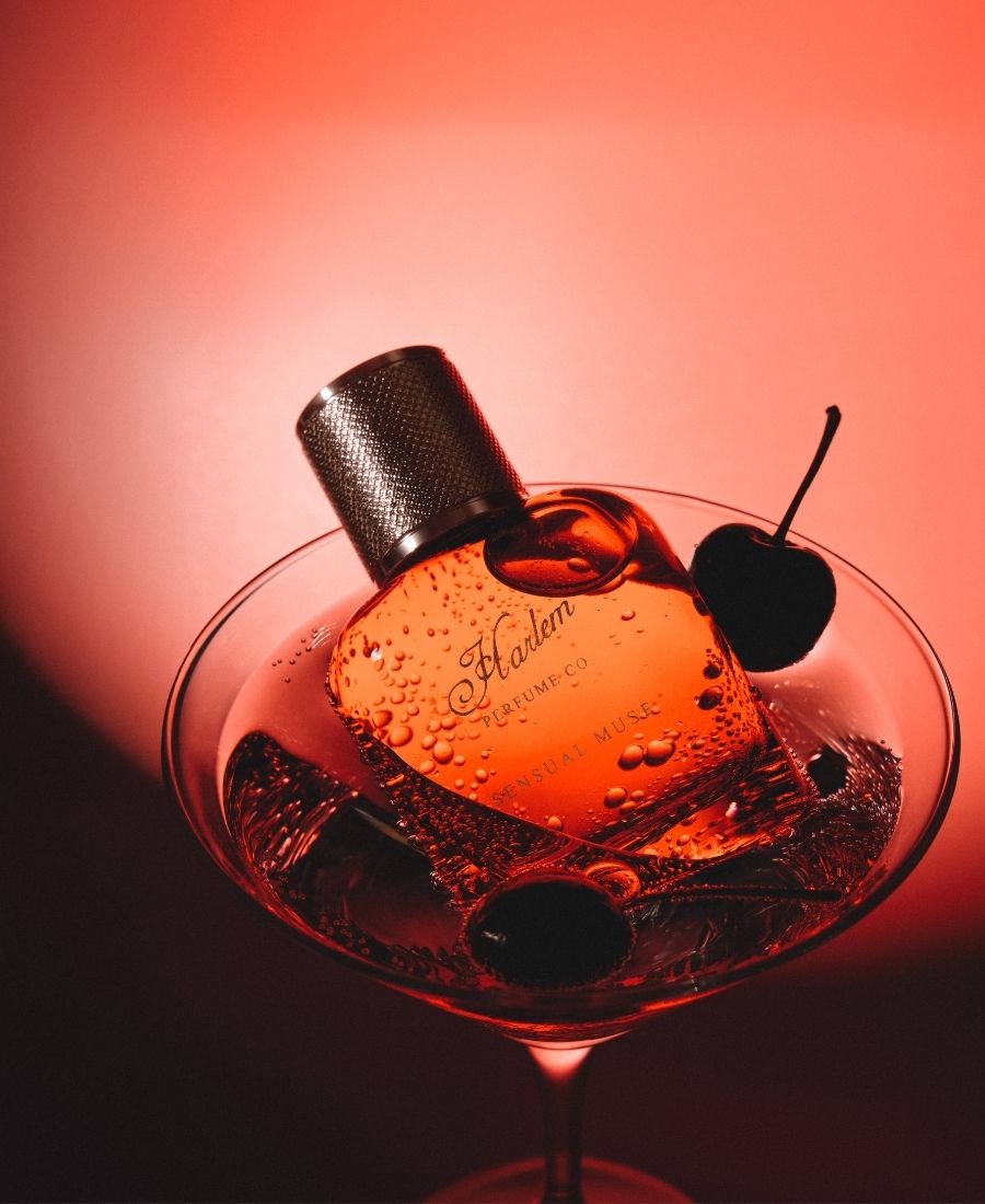 Perfume bottle in a cocktail glass with cherries on a red background