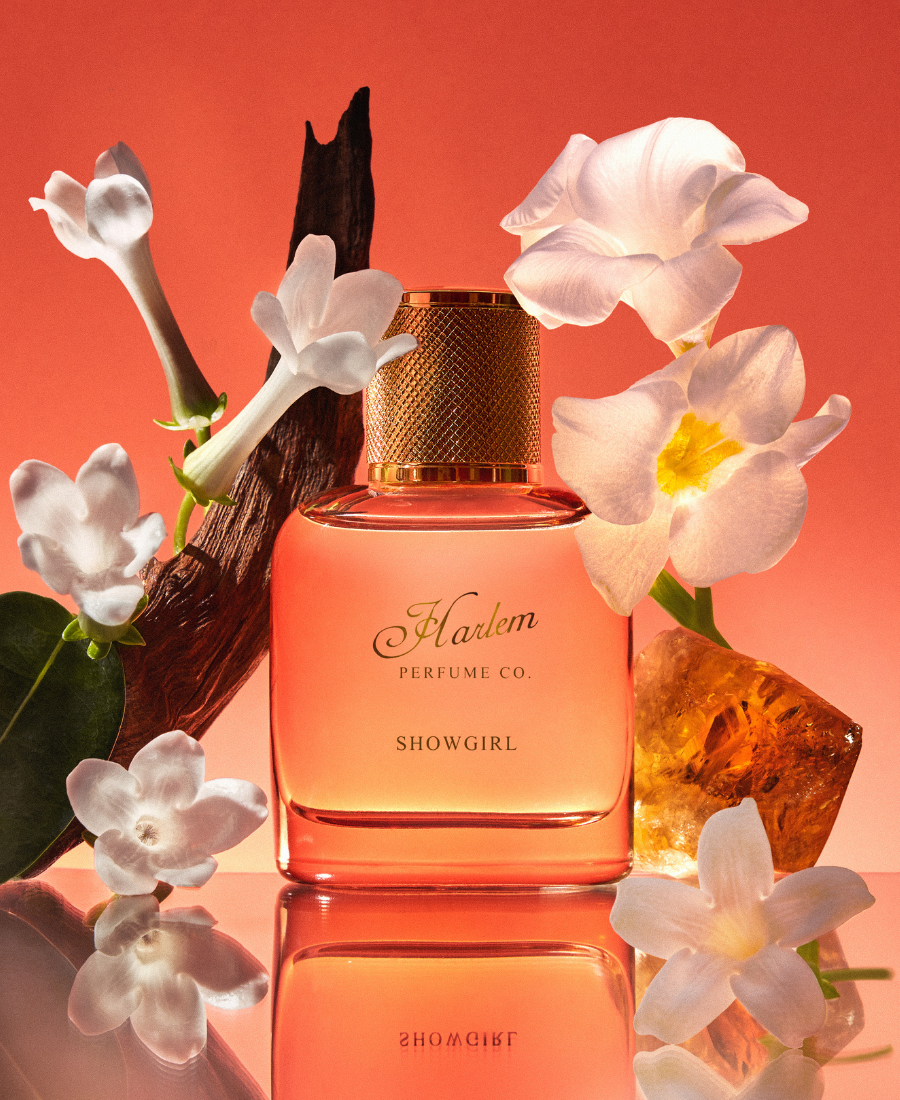 Image of Showgirl Eau de Parfum in a lifestyle setting.  There are jasmine petals and amber surrounding the bottle.