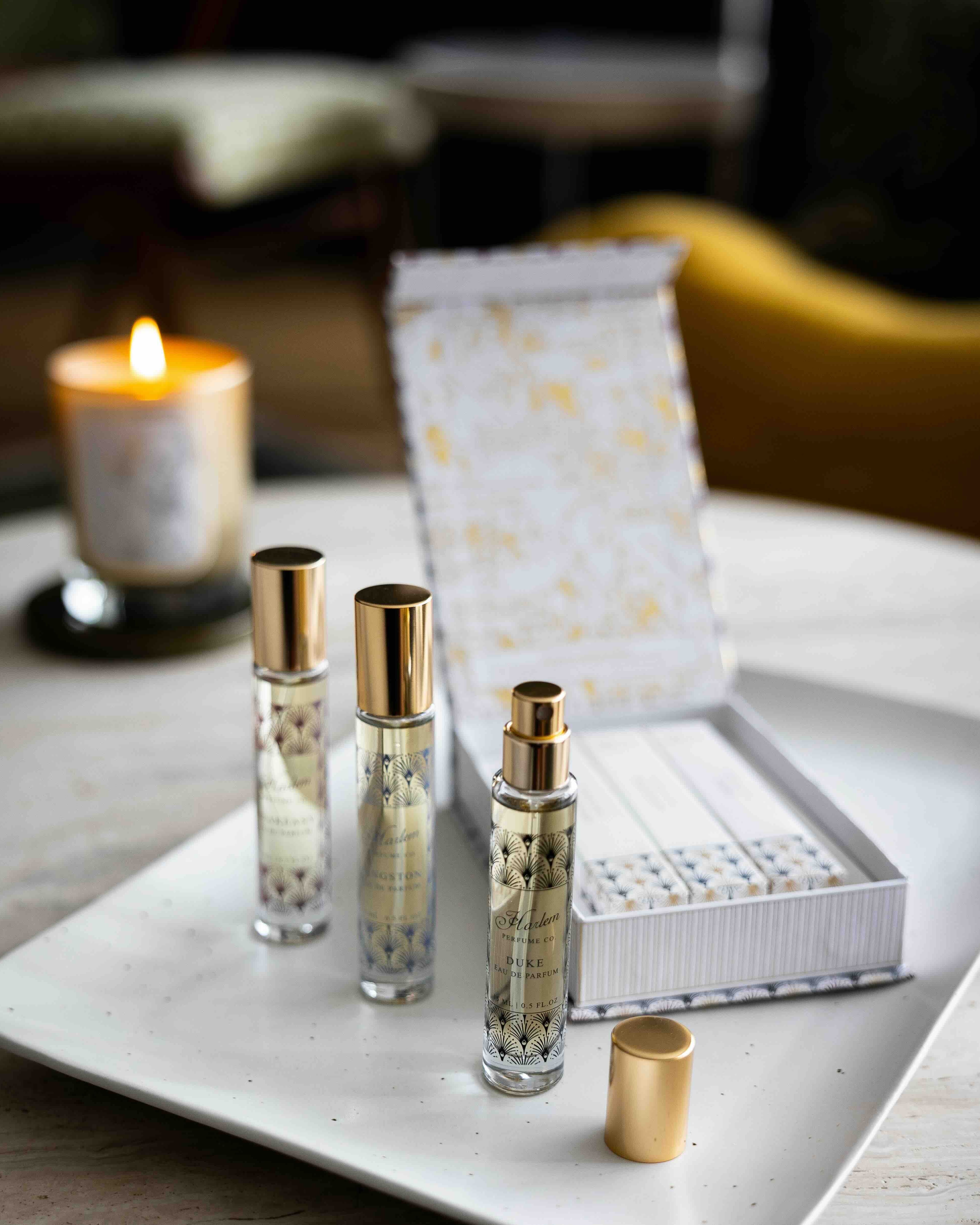 This is a lifestyle image of the perfume discovery box that contains the Langston, Duke and Speakeasy fragrances.  There is a candle burning in the background.